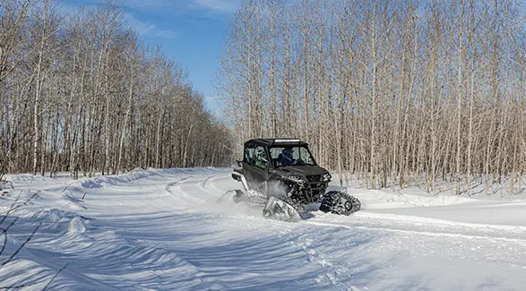 A 2026 Polaris GENERAL XP 1000 crossover side-by-side with tracks installed cruising on a snow-covered trail.