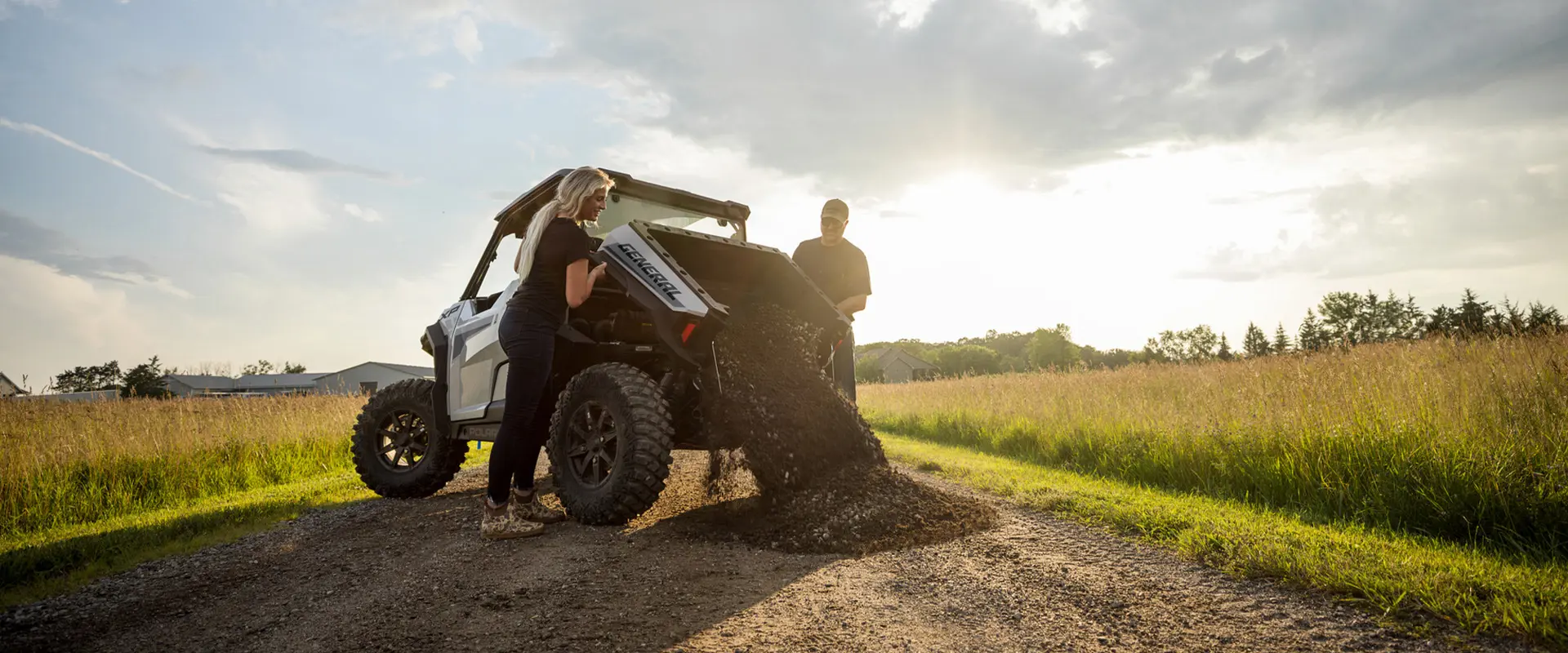 A couple dumping gravel out of the cargo box of their 2026 Polaris GENERAL XP 1000 crossover side-by-side.