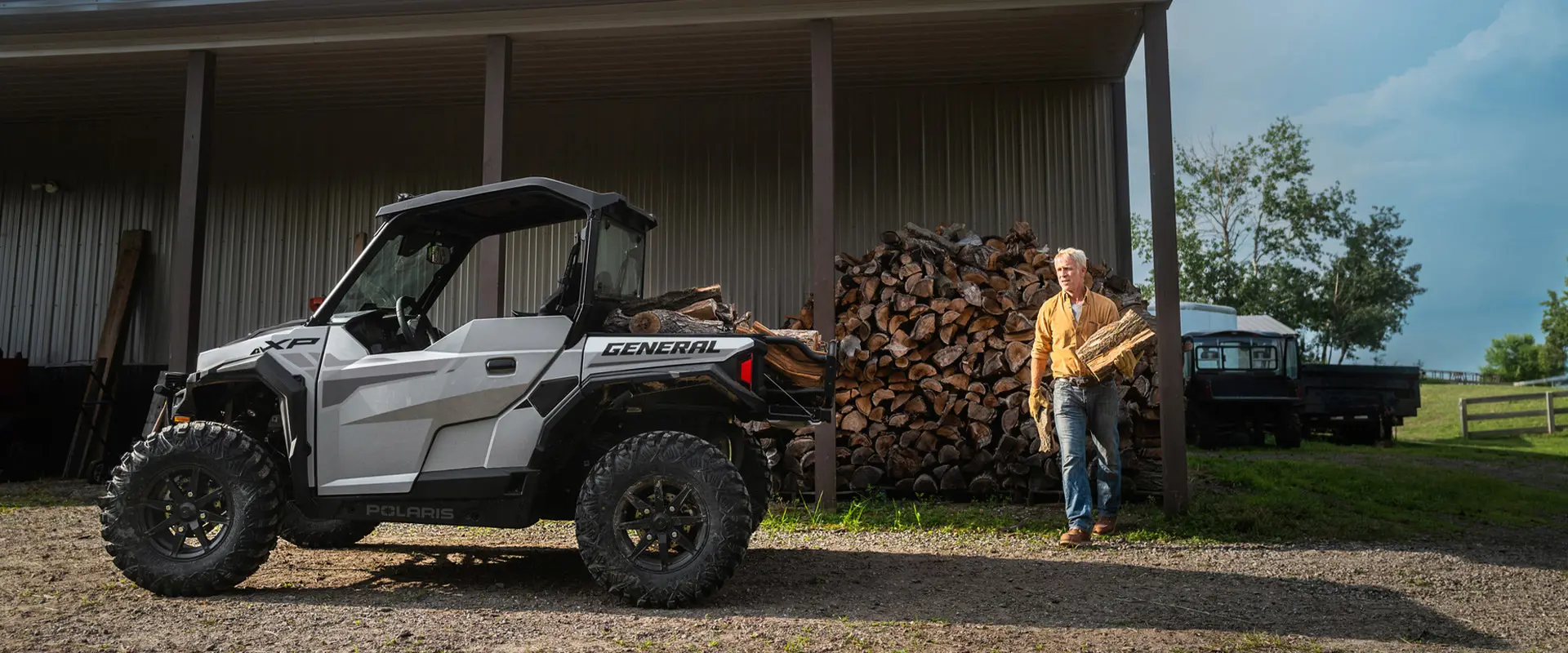 Man loading firewood into the cargo box of his 2026 Polaris GENERAL XP 1000 Sport crossover side-by-side.
