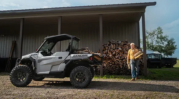 Man loading firewood into the cargo box of his 2026 Polaris GENERAL XP 1000 Sport crossover side-by-side.
