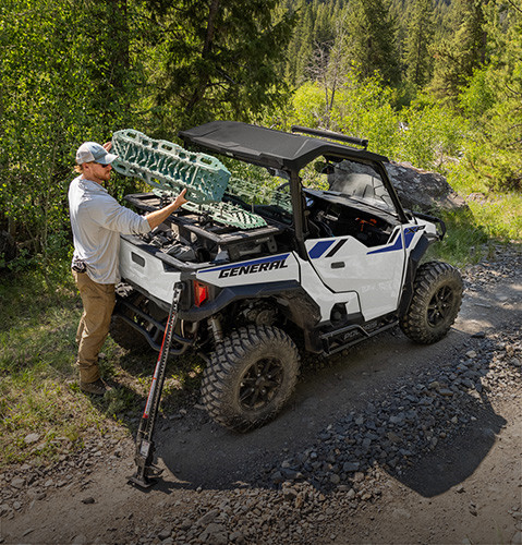 A man grabbing gear from the versatile cargo box of his Polaris GENERAL 1000 crossover side-by-side UTV.