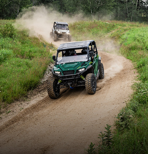 Two Polaris GENERAL XP 1000 crossover side-by-side UTVs comfortably driving on a sandy trail.