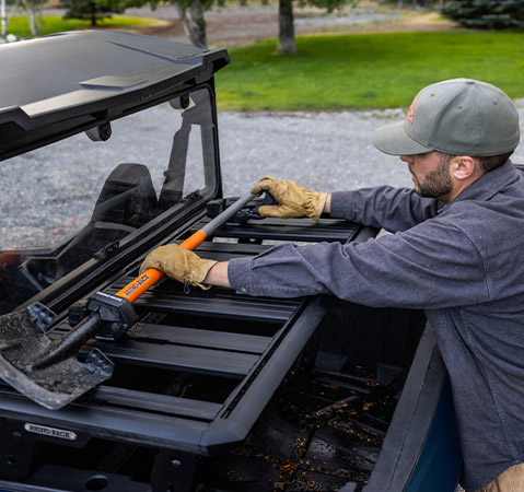 Man grabbing a shovel from the cargo box of his 2027 Polaris GENERAL 1000 side-by-side.