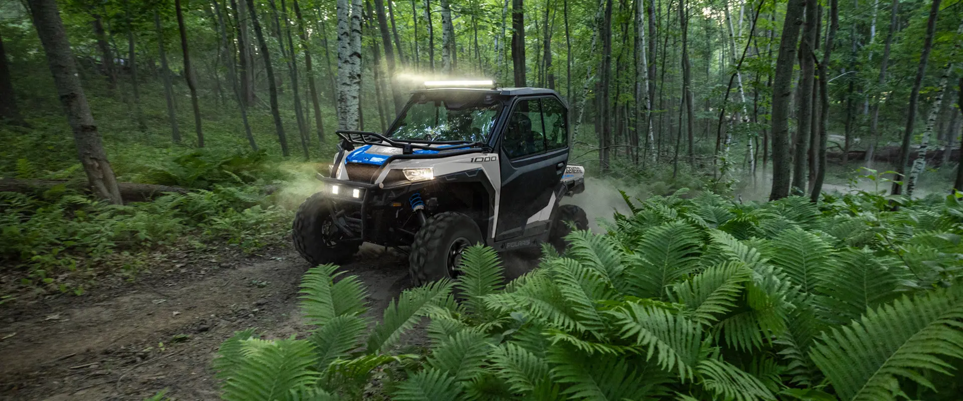 A 2027 Polaris GENERAL 1000 side-by-side driving through the forest with illuminated lights.
