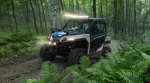 A 2027 Polaris GENERAL 1000 side-by-side driving through the forest with illuminated lights.