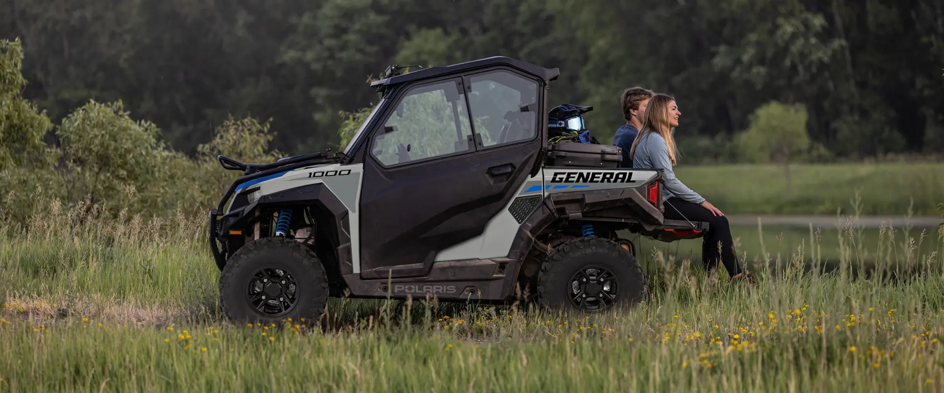 2 people sitting on the tail gate of a 2027 Polaris GENERAL 1000 side-by-side.