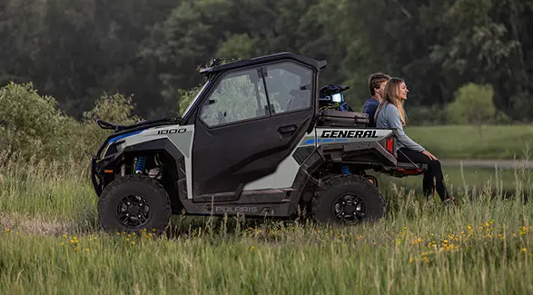 2 people sitting on the tail gate of a 2027 Polaris GENERAL 1000 side-by-side.