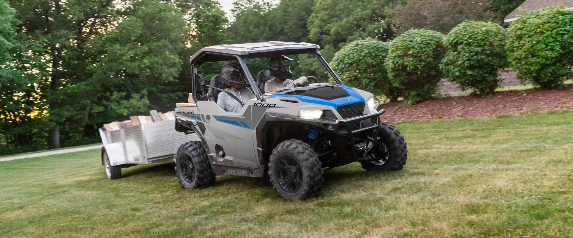 2 riders in a 2027 Polaris GENERAL 1000 side-by-side pulling a loaded trailer across the lawn.
