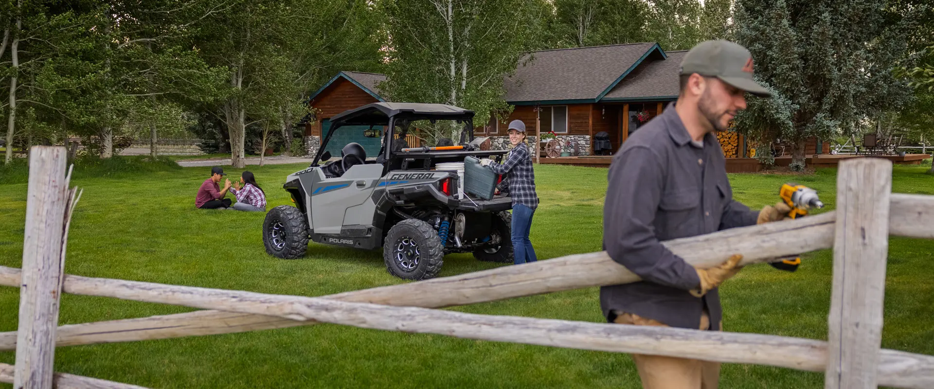 A couple using gear from the cargo box of their 2027 Polaris GENERAL 1000 side-by-side to fix a fence on their property.