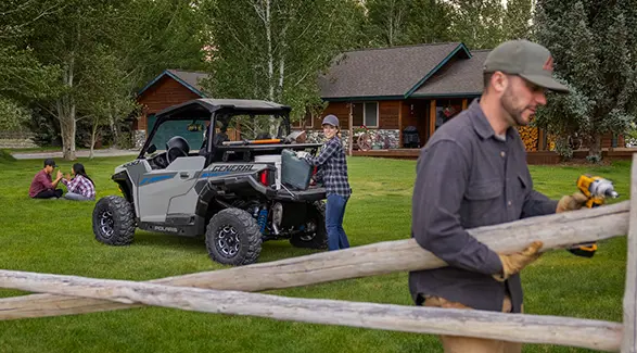 A couple using gear from the cargo box of their 2027 Polaris GENERAL 1000 side-by-side to fix a fence on their property.