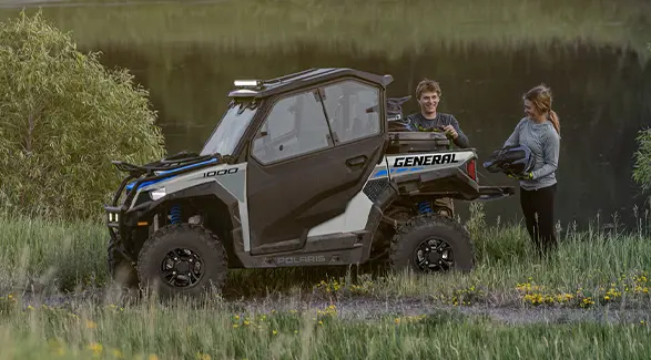 2 young adults grabbing their helmets to ride their 2027 Polaris GENERAL 1000 side-by-side.