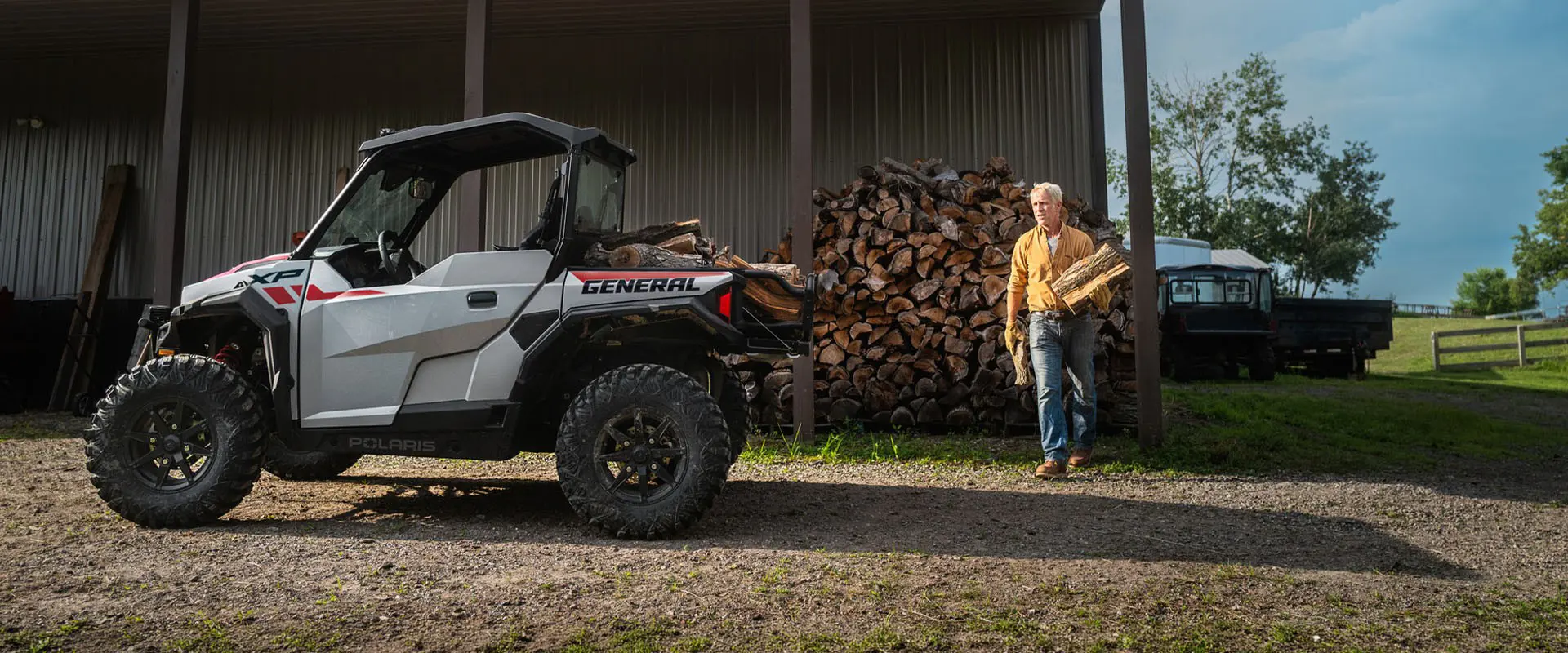 A man loading firewood into the cargo box of a 2027 Polaris GENERAL XP 1000 SxS.