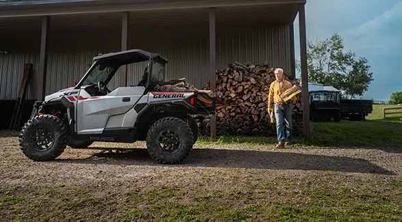 A man loading firewood into the cargo box of a 2027 Polaris GENERAL XP 1000 SxS.