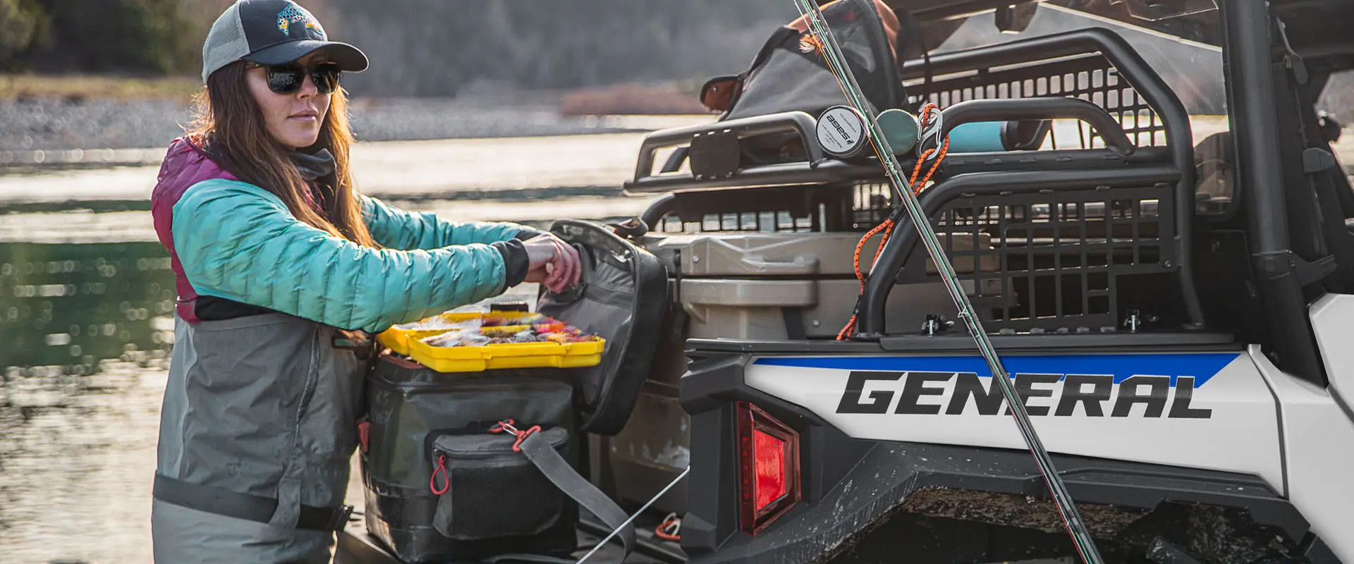 A woman getting fishing tackle from the cargo box of her 2027 Polaris GENERAL XP 1000 side by side.