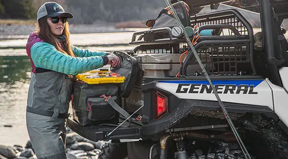 A woman getting fishing tackle from the cargo box of her 2027 Polaris GENERAL XP 1000 side by side.