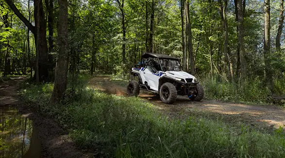 2 riders in a 2027 Polaris GENERAL XP 1000 side by side enjoying a forested trail ride on a beautiful day.