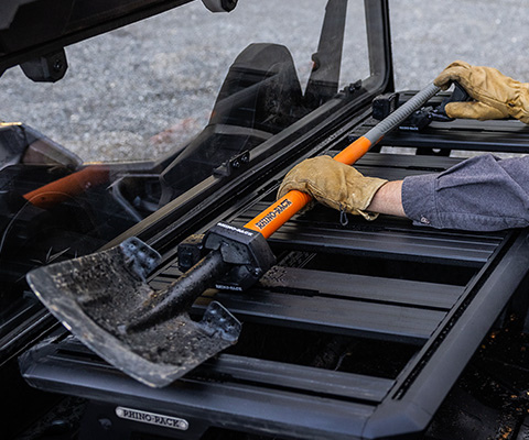 A man pulling a shovel from the Rhino rack accessory mounted on the back of his General