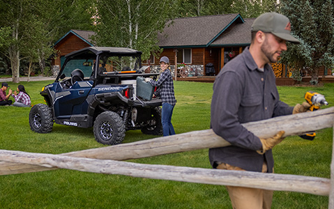 A man drilling in a fence while a woman unloads tools from the cargo bed of their General