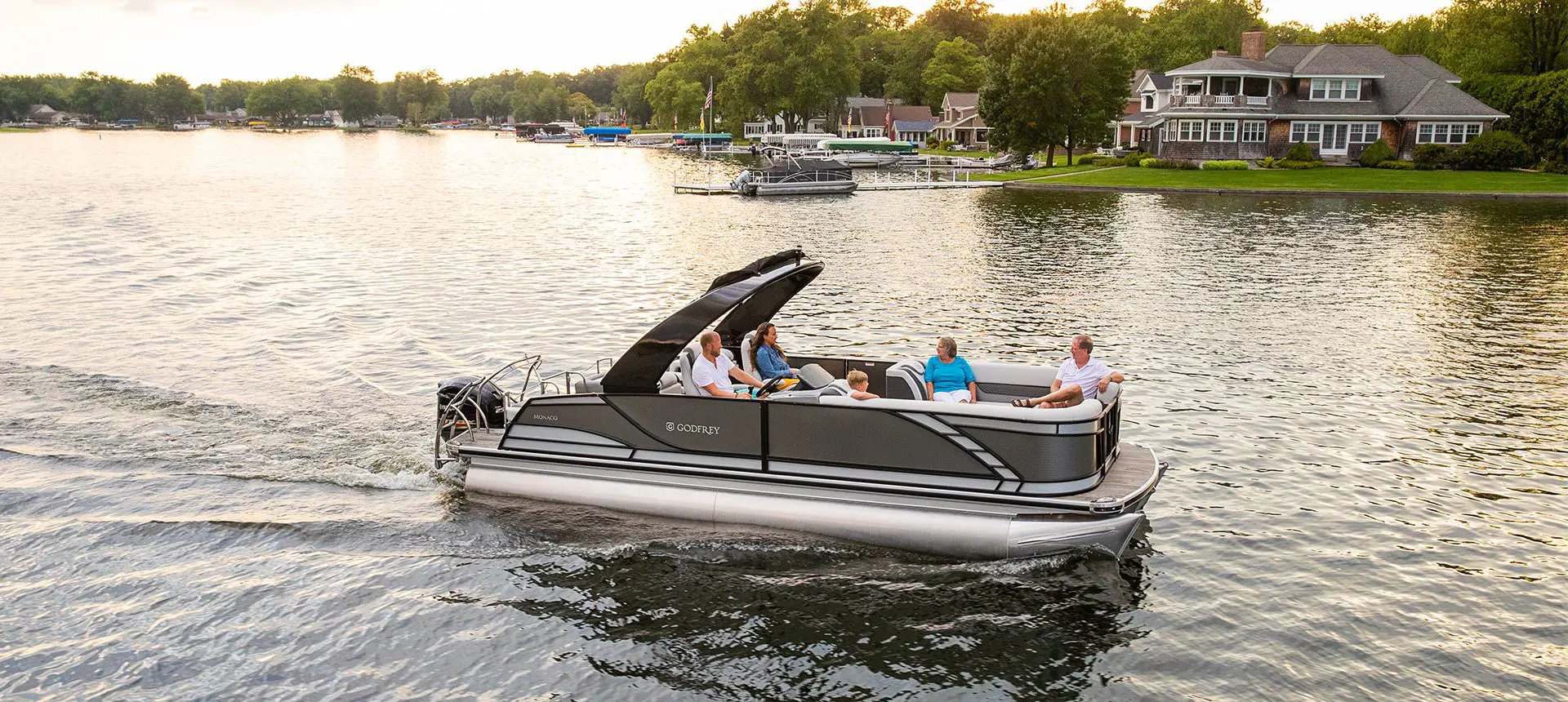 Side profile of a Godfrey Monaco Lounge pontoon boat cruising on a lake.