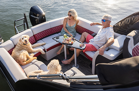 A couple and their dogs relaxing on the Ultra Lounge stern seats on a Godfrey pontoon boat with the Lounge layout.