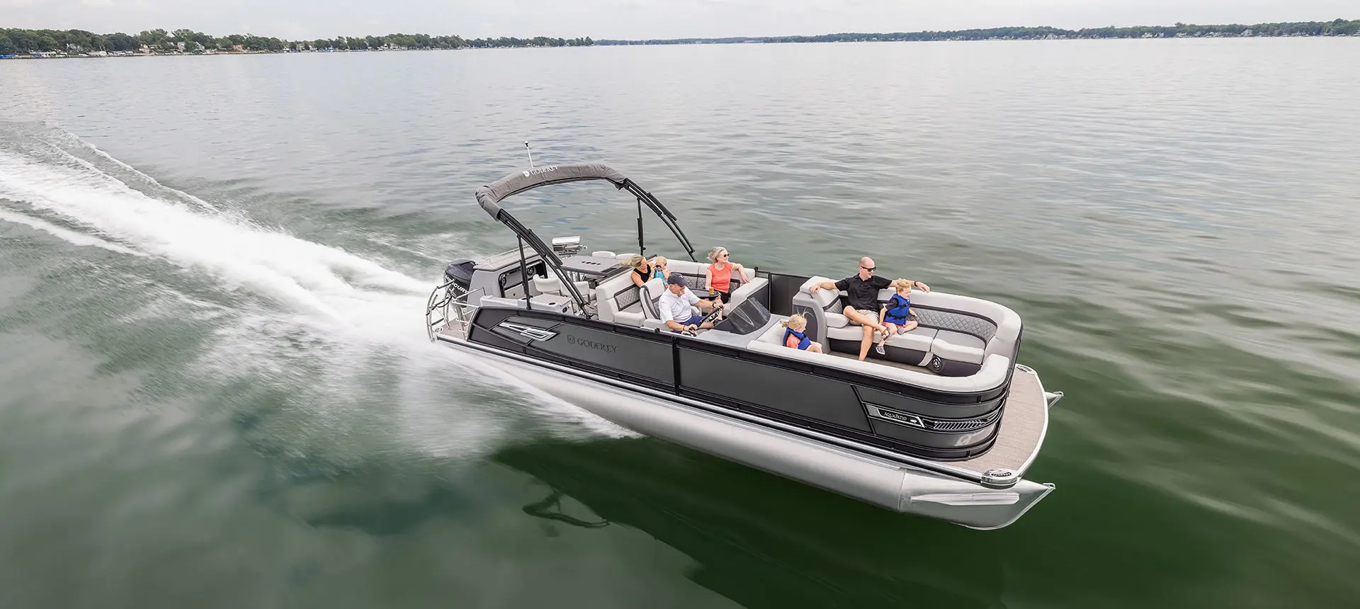 Family speeding across a lake on a Godfrey AquaPatio Entertainment pontoon boat.