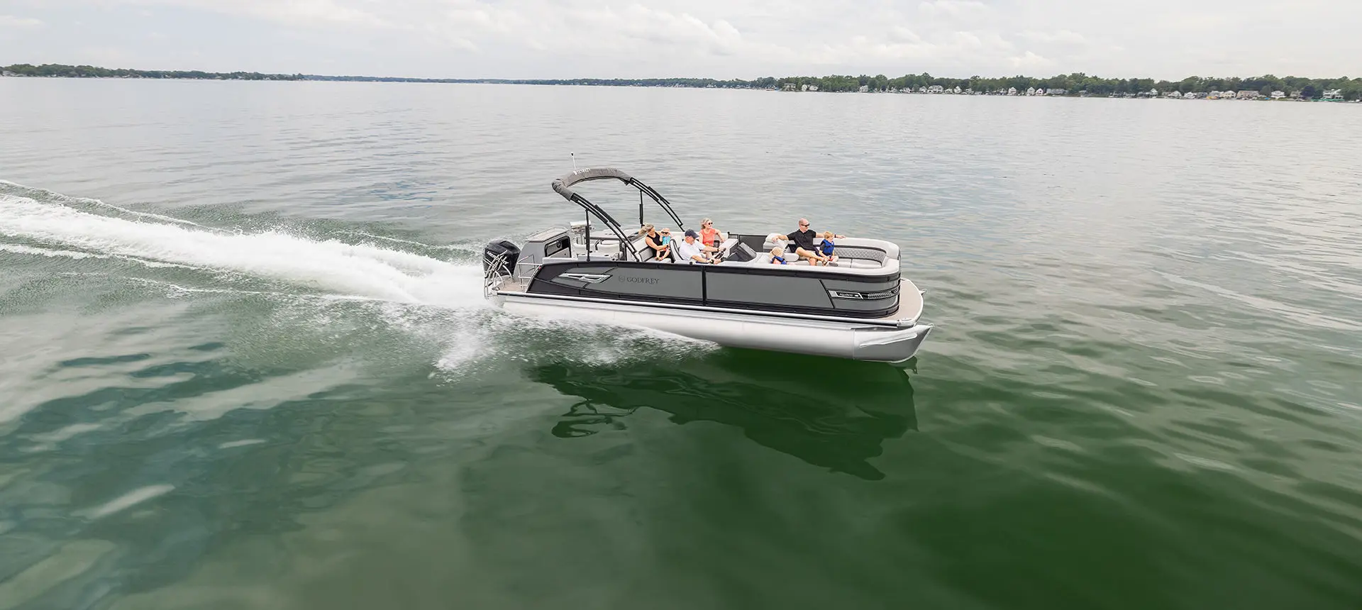 Side view of a Godfrey AquaPatio Entertainment pontoon boat on a lake.
