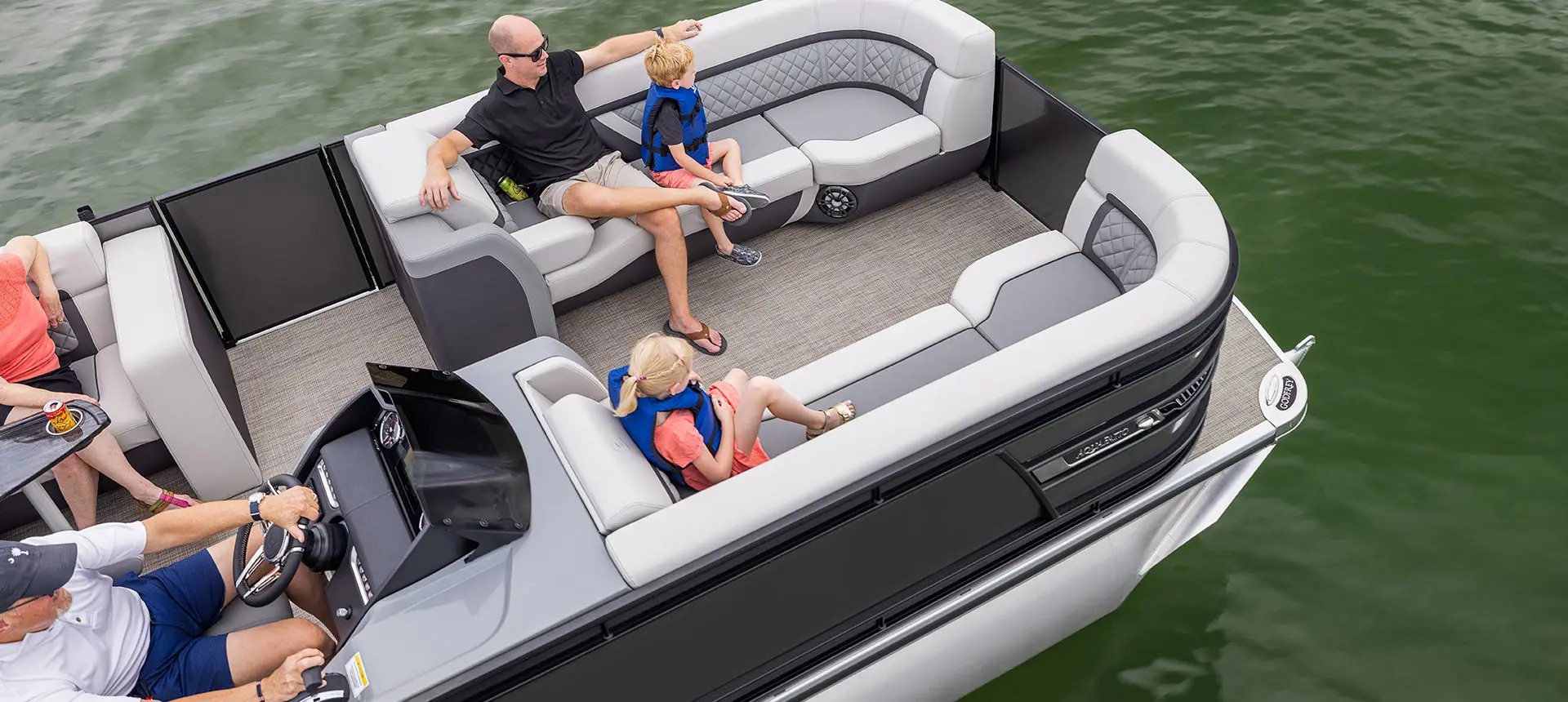 Over head view of a family sitting on the bow split bench seats on a Godfrey AquaPatio Entertainment pontoon boat.