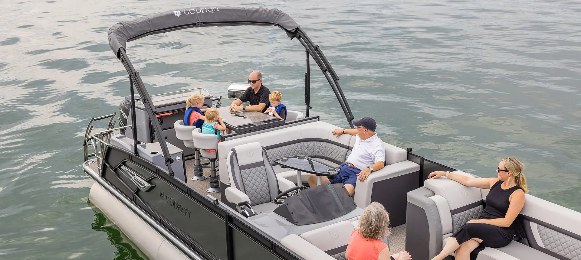 Family relaxing at the table on a Godfrey AquaPatio Entertainment pontoon boat.