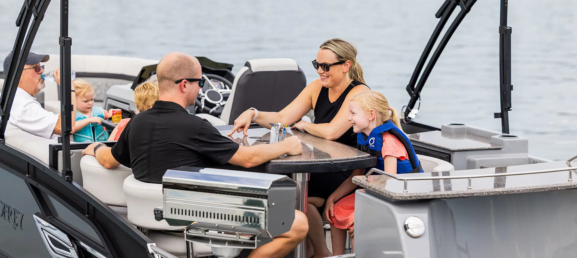 Family having a snack at the stern table on a Godfrey AquaPatio Entertainment pontoon boat.