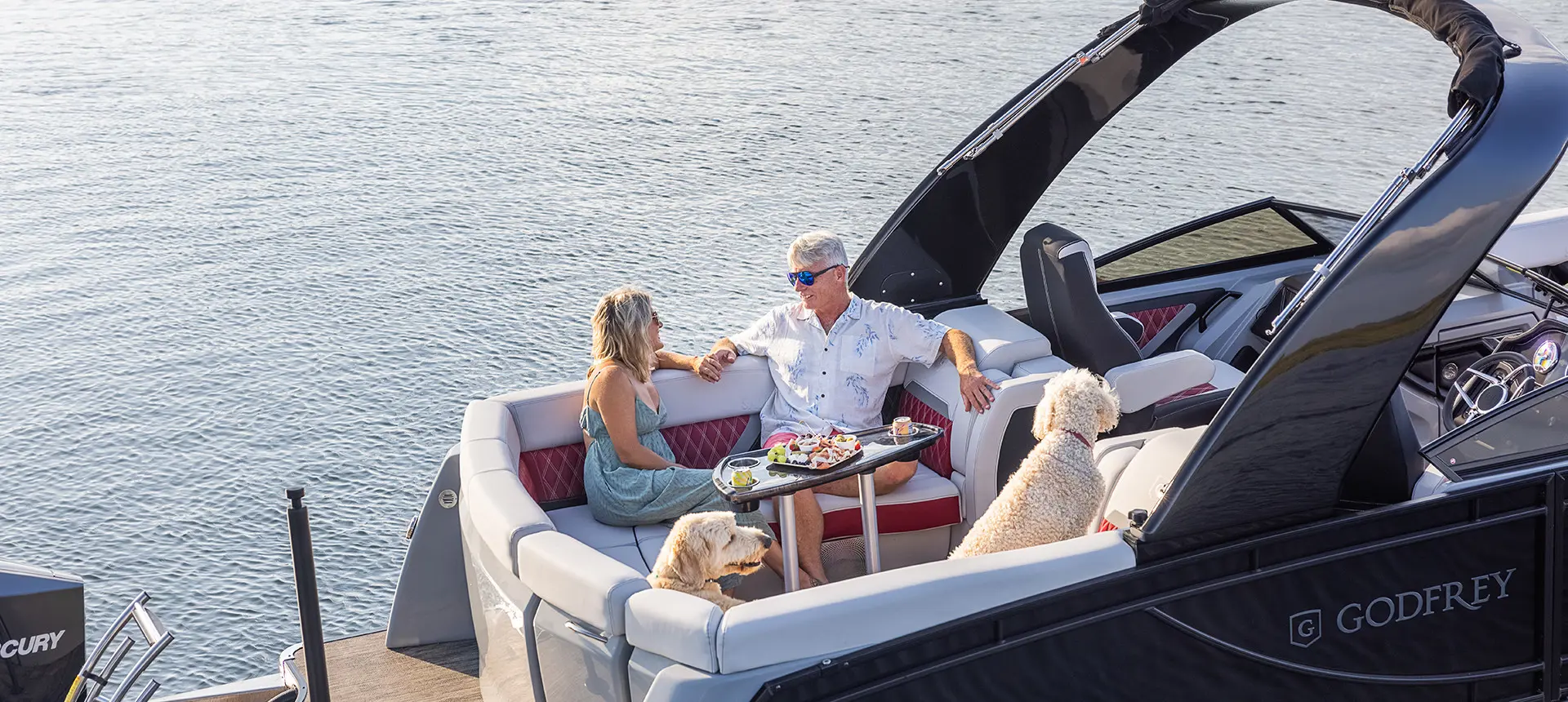 Couple mangeant une collation avec leur chien dans le vaste coin salon arrière d’un ponton Godfrey Sanpan Windshield.