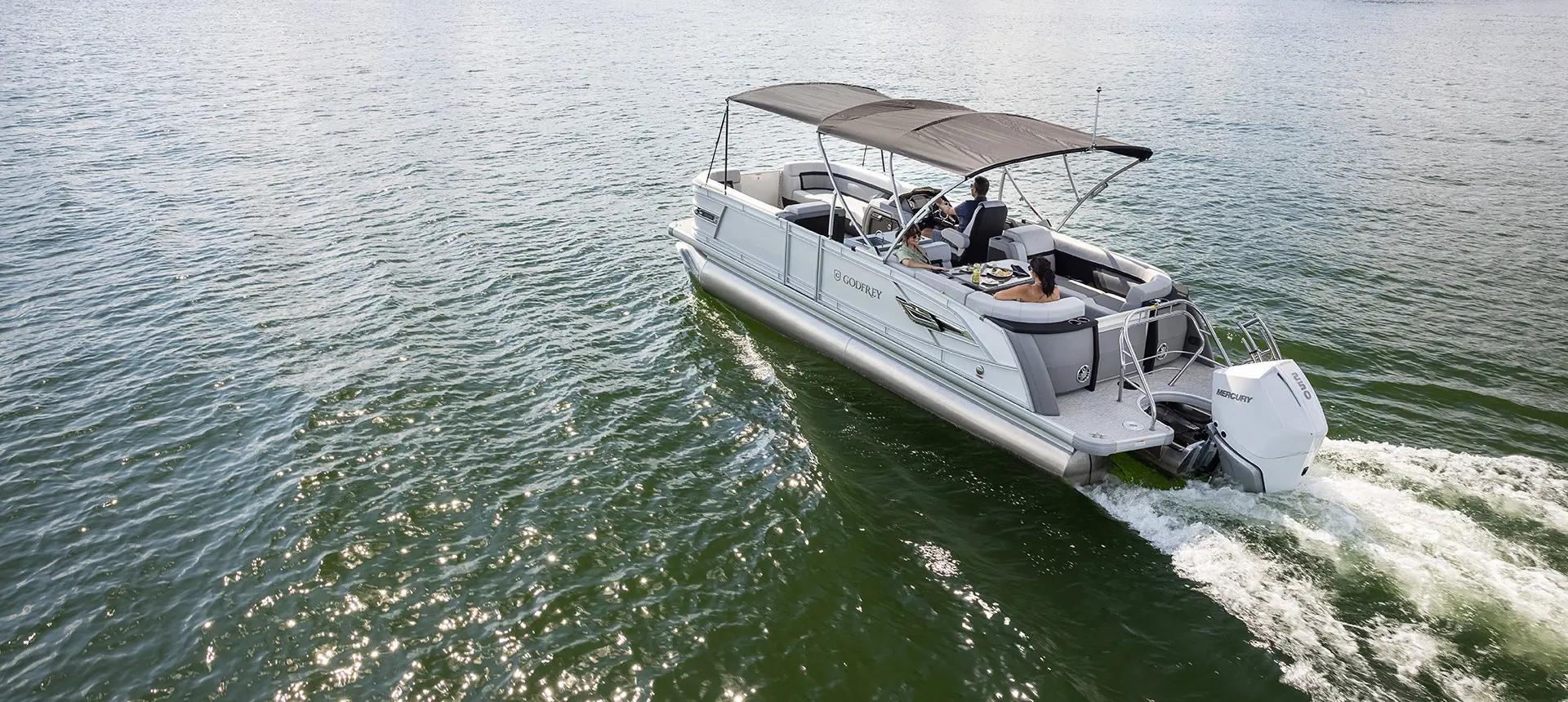 Rear view of a Godfrey AquaPatio Entertainment pontoon boat on a lake with the canopy up.