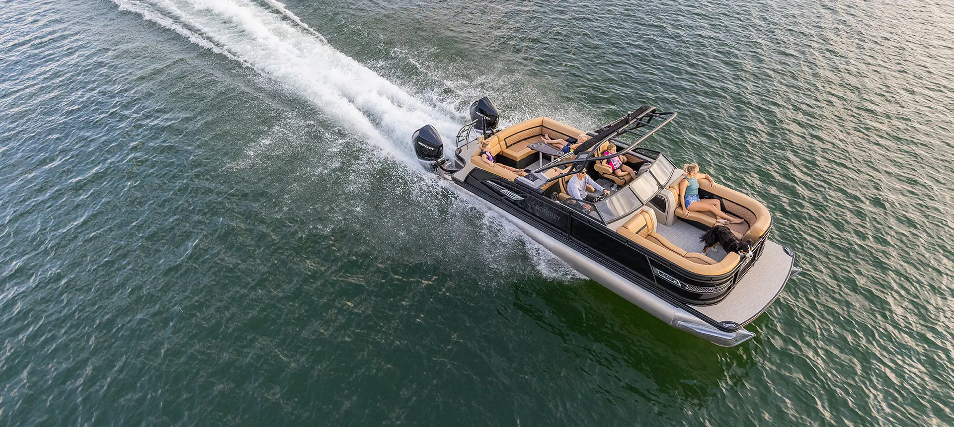 Aerial view of a Godfrey AquaPatio Lounge pontoon boat with twin engines cruising on a lake.