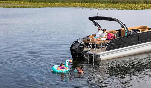 kids swimming by the stern on a godfrey monaco lounge pontoon while their parents watch