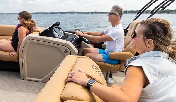 family smiling while driving a godfrey monaco lounge pontoon on a lake