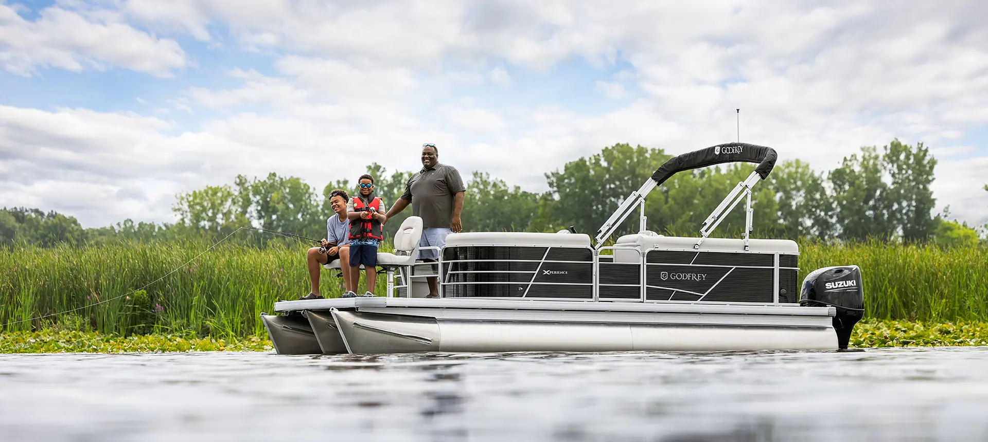 papa pointant à ses fils un point de pêche sur la proue d’un ponton godfrey xperience fishing