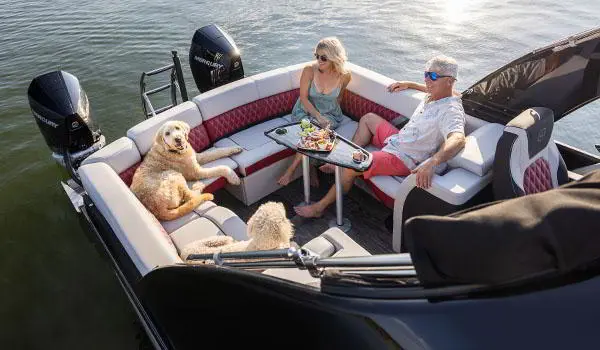 Vue aérienne d’un couple prenant une collation avec leurs chiens dans le vaste coin salon à la poupe d’un ponton Godfrey Sanpan Lounge 2700 ULW Twin.