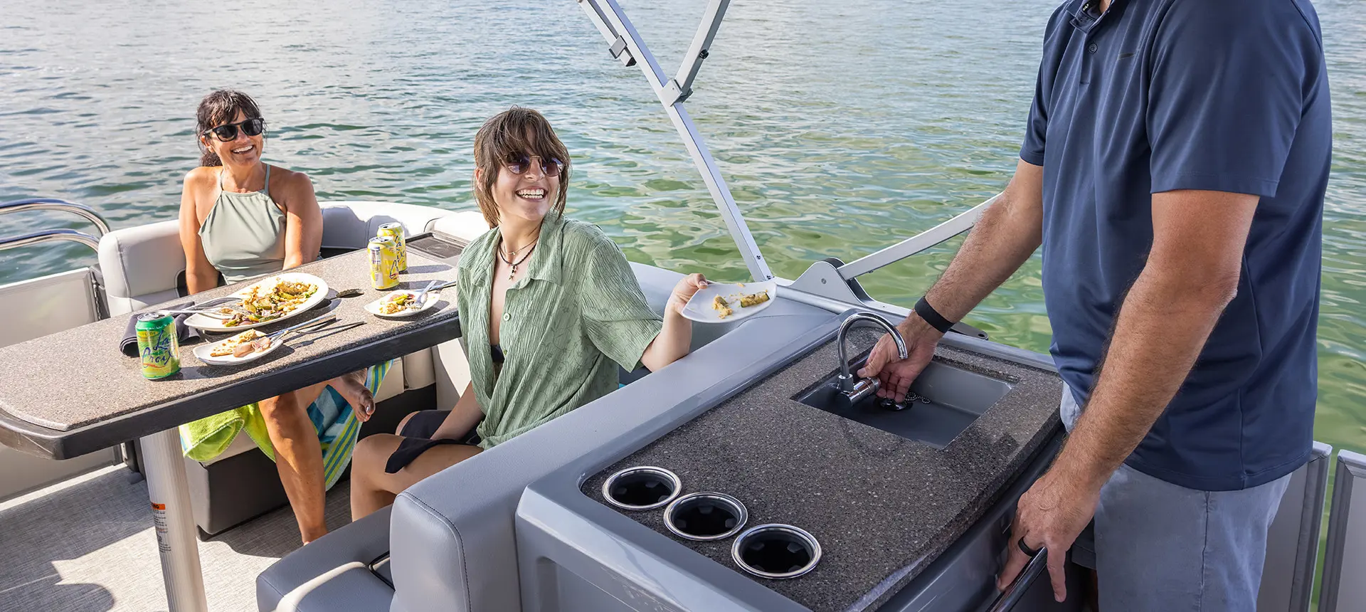 woman handing a dirty plan to a man standing at the sink on a godfrey aquapatio series pontoon
