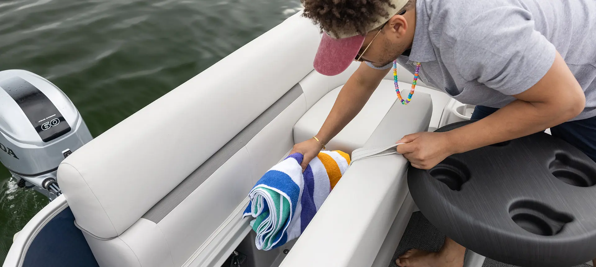 man getting a towel from the in seat storage on a godfrey xperience split bench pontoon