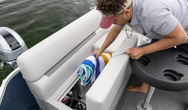 man getting a towel from the in seat storage on a godfrey xperience split bench pontoon