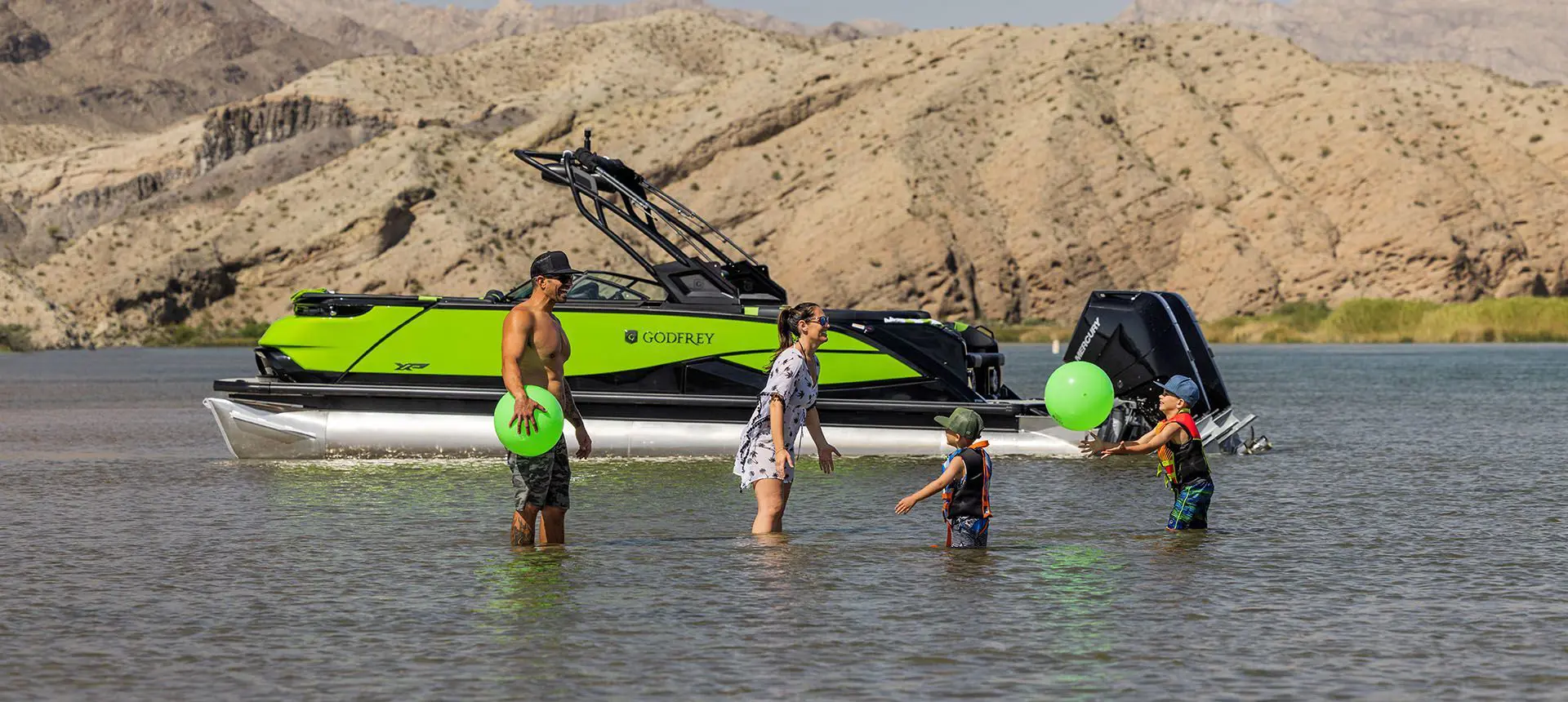 Family playing near shore while their Godfrey XP Tritoon boat floats in the background.