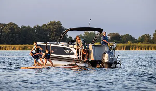 kids playing on a stand up paddle board near a godfrey aquapatio entertainment pontoon on a lake