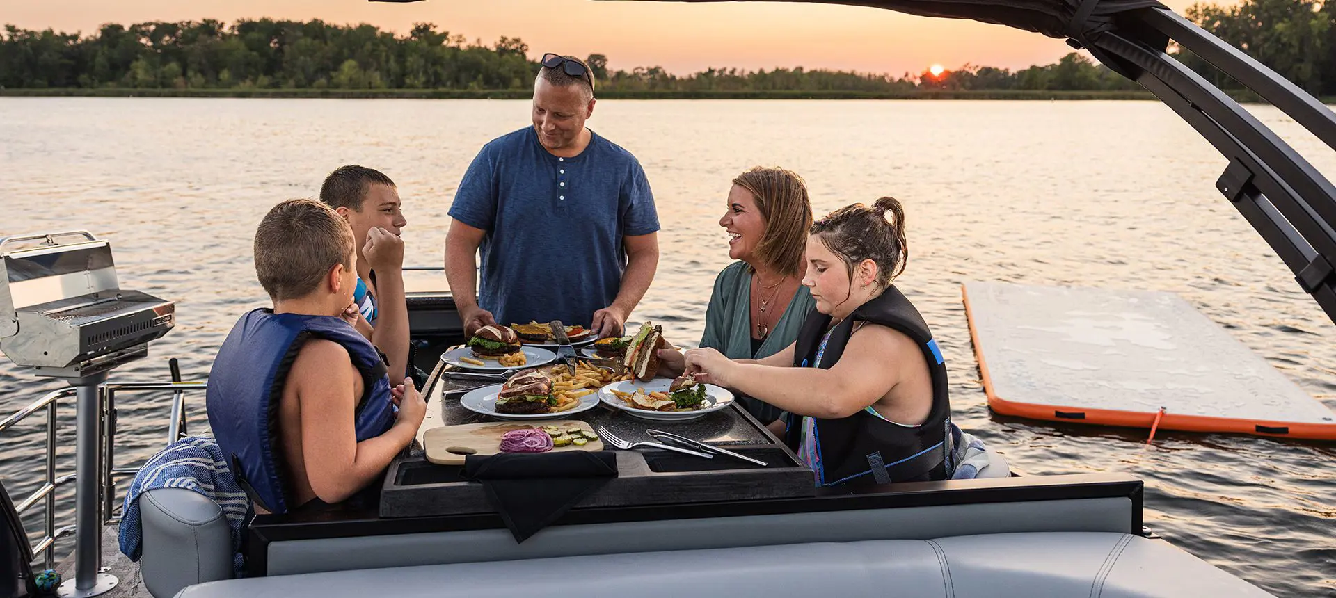 Family eating at the stern table on a Godfrey AquaPatio Entertainment pontoon boat.