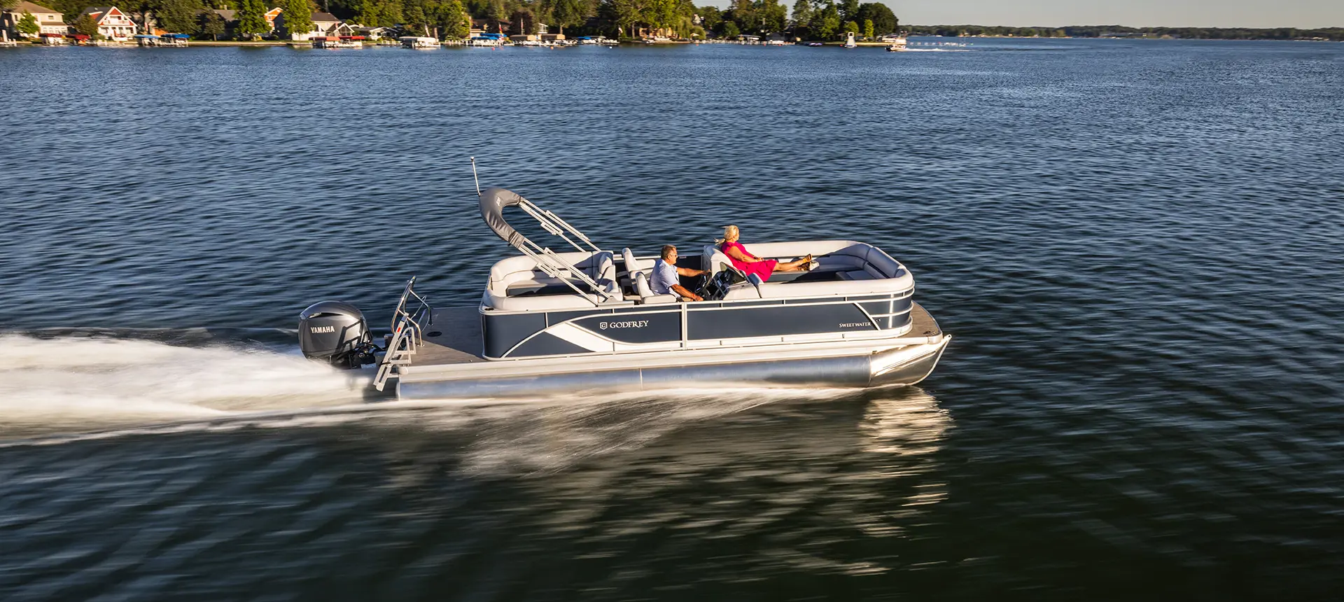 side view of a godfrey sweetwater split bench pontoon cruising across a lake