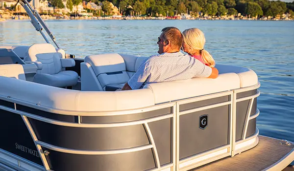 couple relaxing on the bow of a godfrey sweetwater split bench pontoon