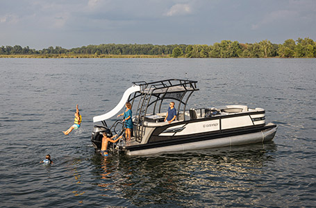 Kids using the Sundeck slide while parents watch from the stern of a Godfrey pontoon boat with the Entertainment layout.