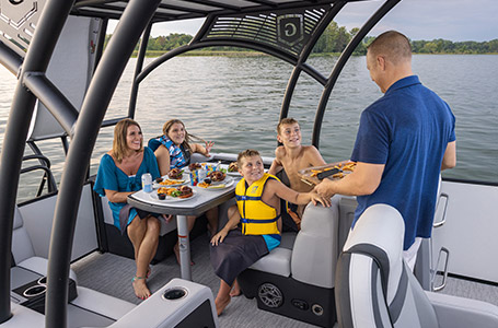 A family relaxing under the shaded sundeck of a Godfrey pontoon boat with the Sundeck layout.