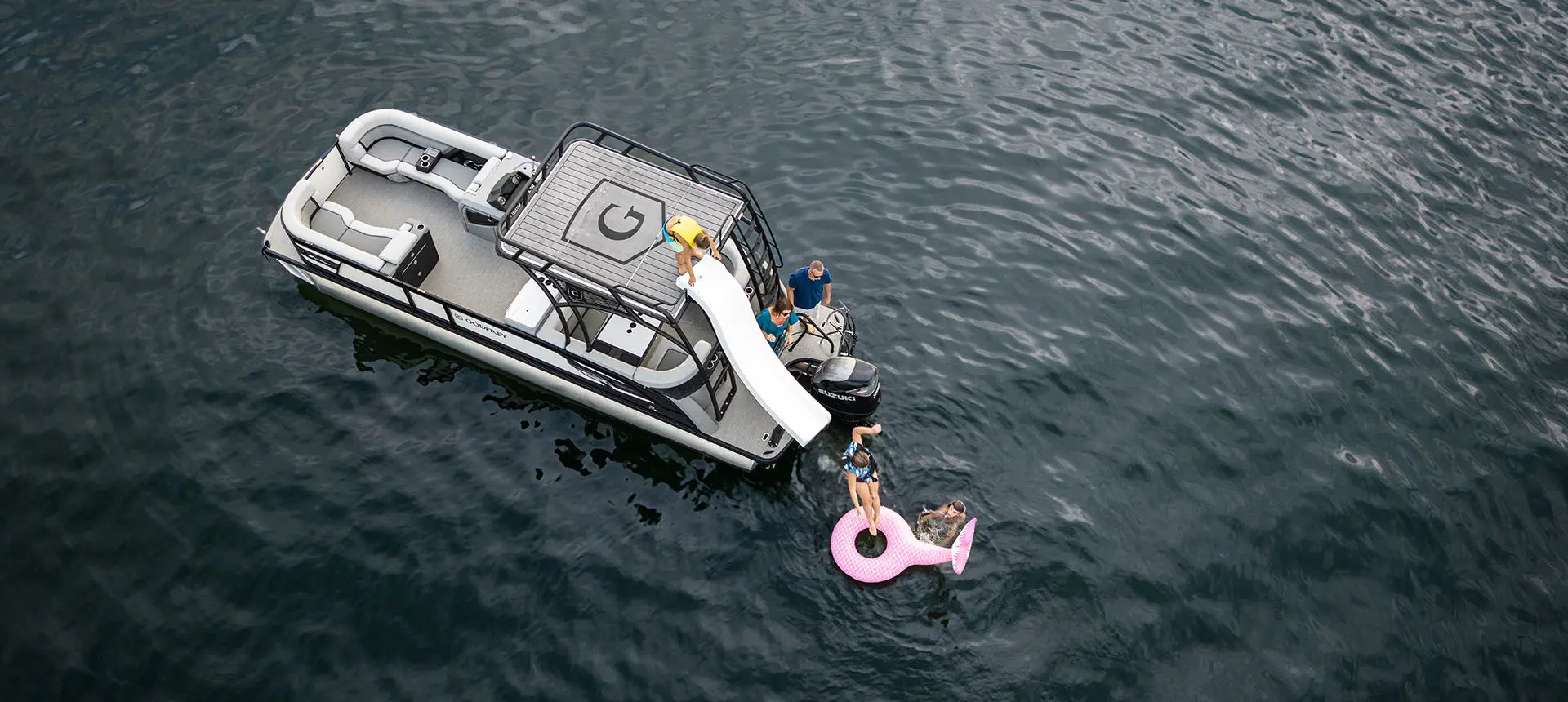 Aerial view of a kid going down the slide on a Godfrey AquaPatio Entertainment pontoon boat.