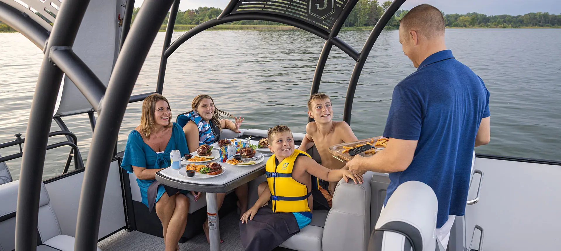 Family having a snack at the stern table on a Godfrey AquaPatio Entertainment pontoon boat.