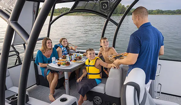 Family having a snack at the stern table on a Godfrey AquaPatio Entertainment pontoon boat.