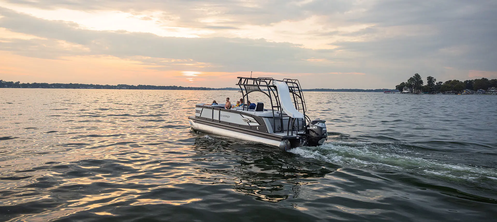 Far away view of a Godfrey AquaPatio Entertainment pontoon boat cruising on a lake.